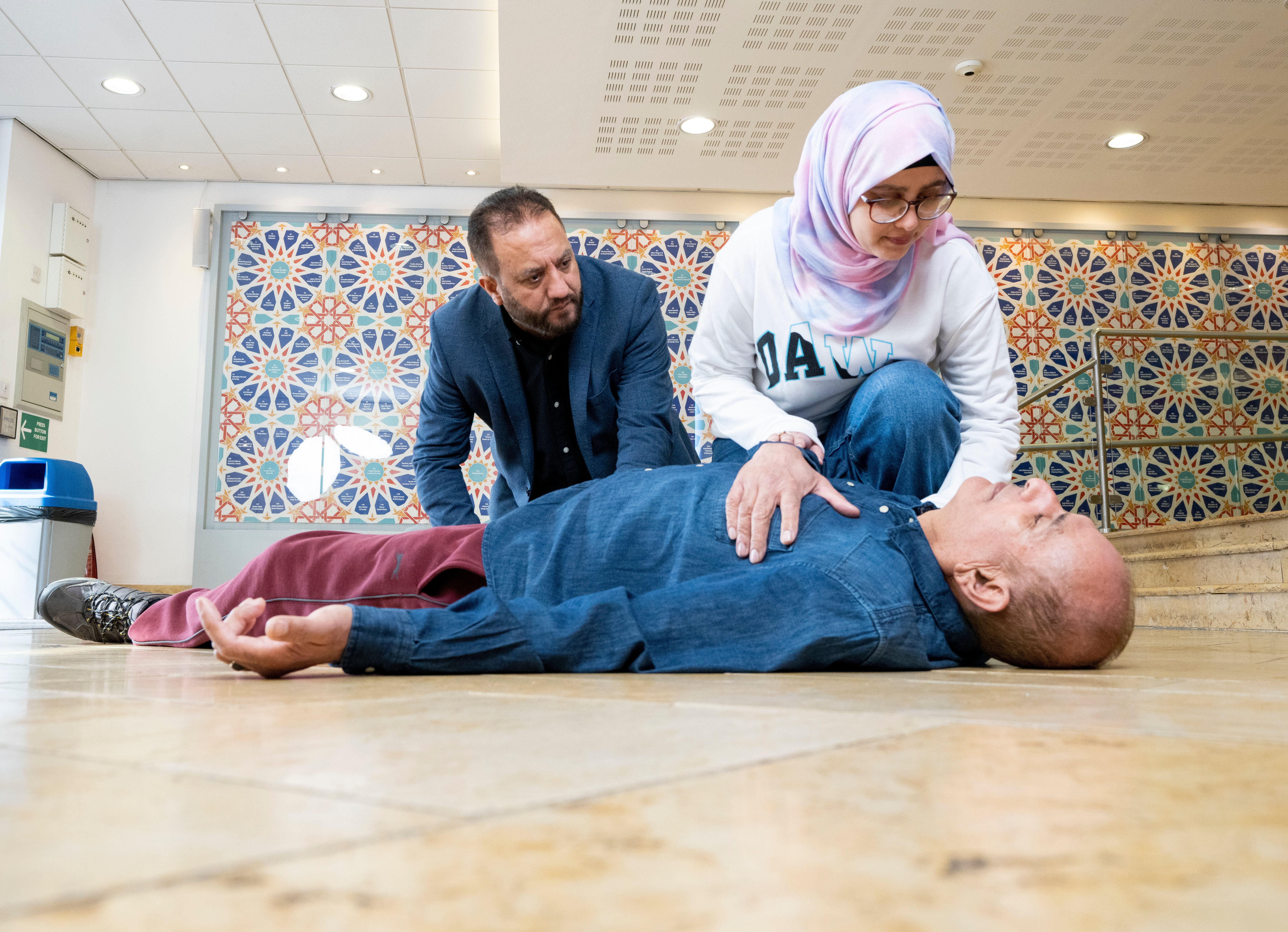 A man and woman kneeling over someone lying on the floor.